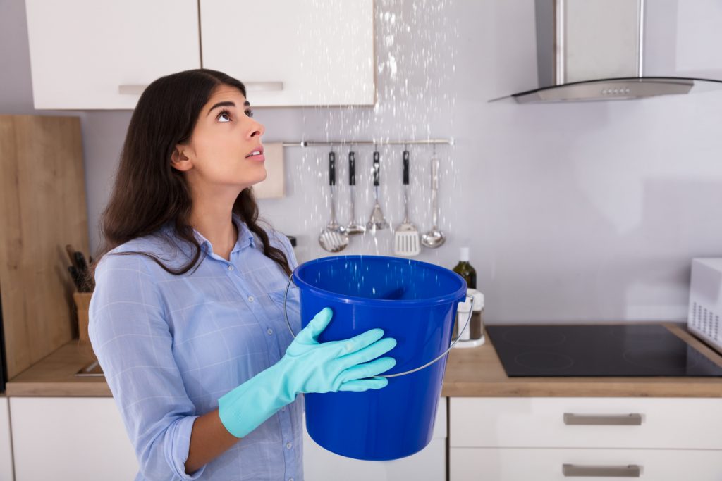 woman holding bucket while water leaks from the roof.