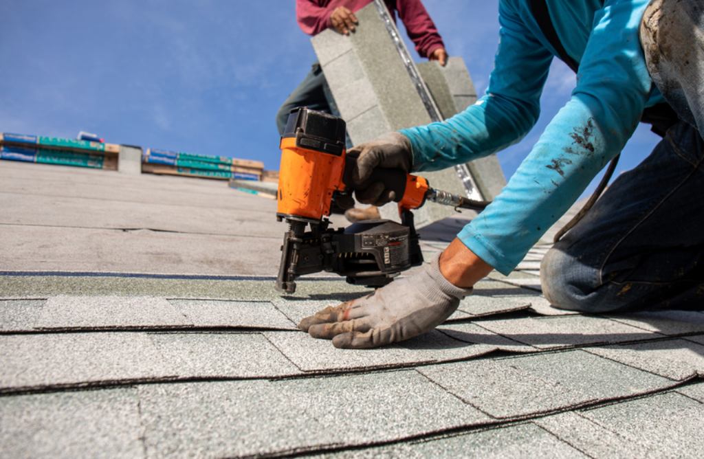 A roofer uses a nail gun to secure shingles down on a customer's roof.