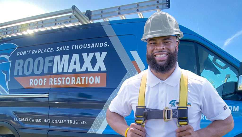 A Roof Maxx dealer smiles in front of a blue van with branded Roof Maxx wrap