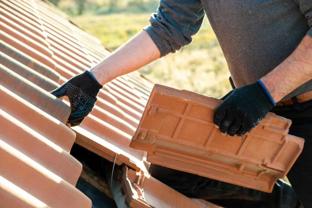 A roofer removes and reinstalls clay tiles on a roof