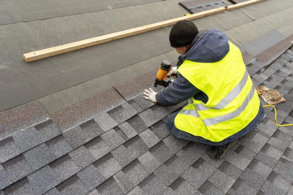 A man in a reflective vest nails shingles down onto a roof