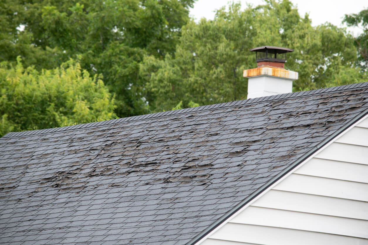 A badly damaged asphalt shingle roof with lifting, peeling, and missing shingles