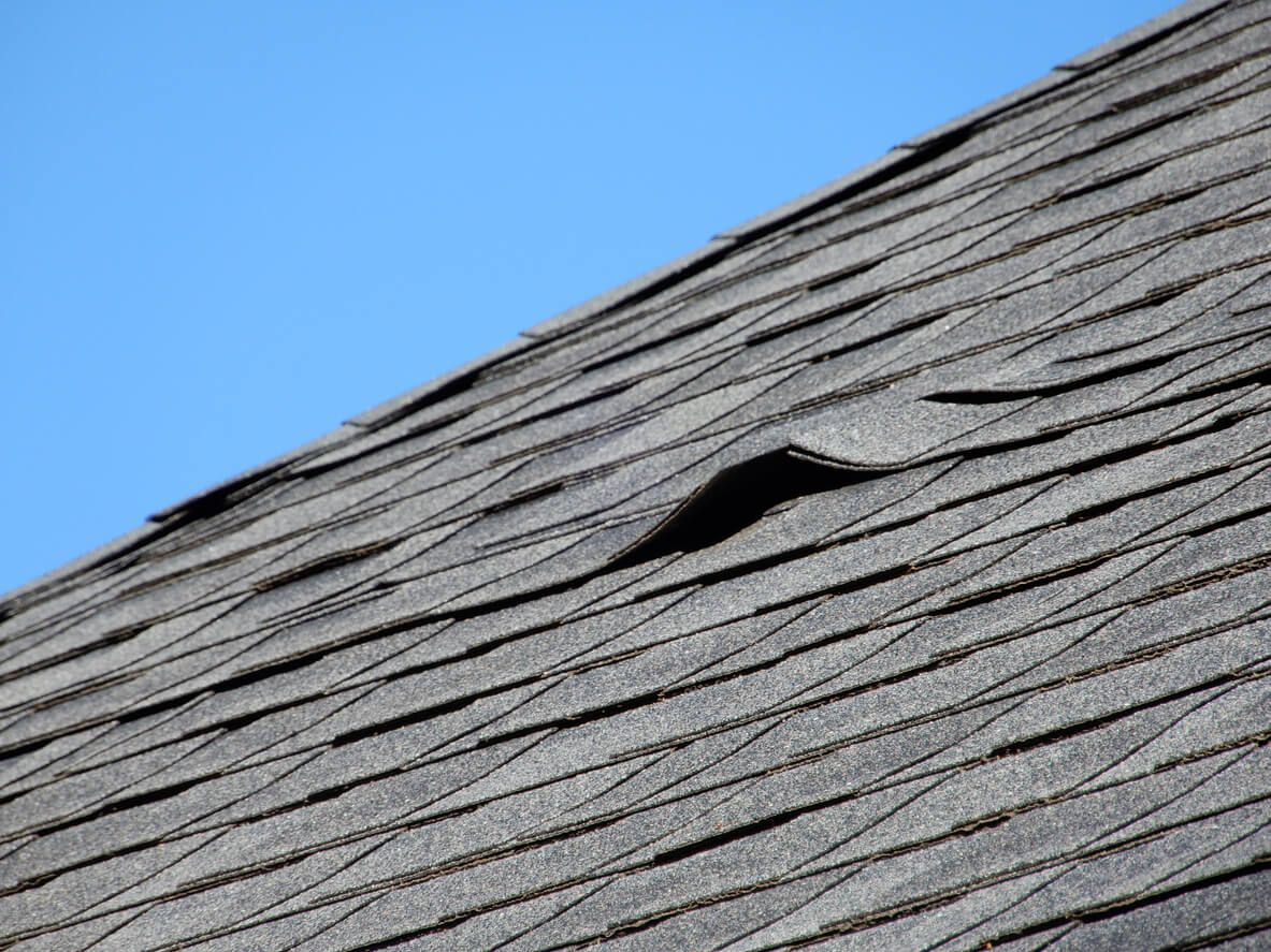 Cracked and broken shingles lifting up and away from an asphalt shingle roof