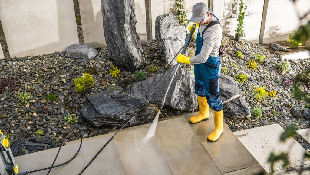 A worker power washes a customer's concrete flagstone pathway
