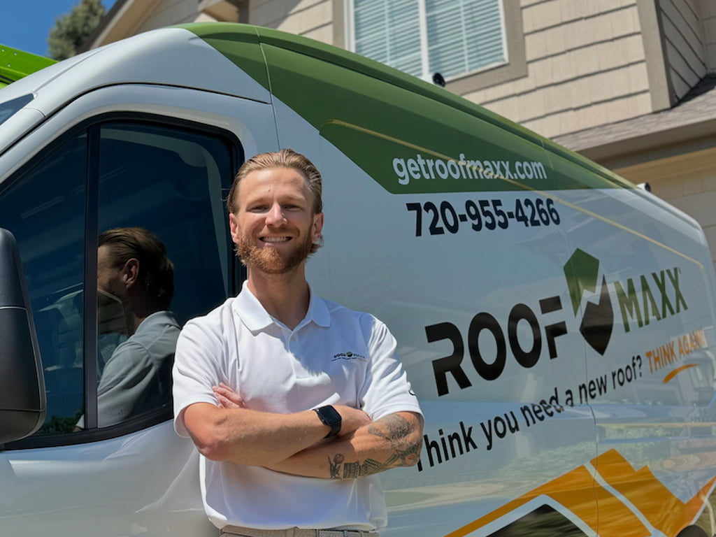 Roof Maxx dealer Jacob Elhart stands smiling beside a branded Roof Maxx truck