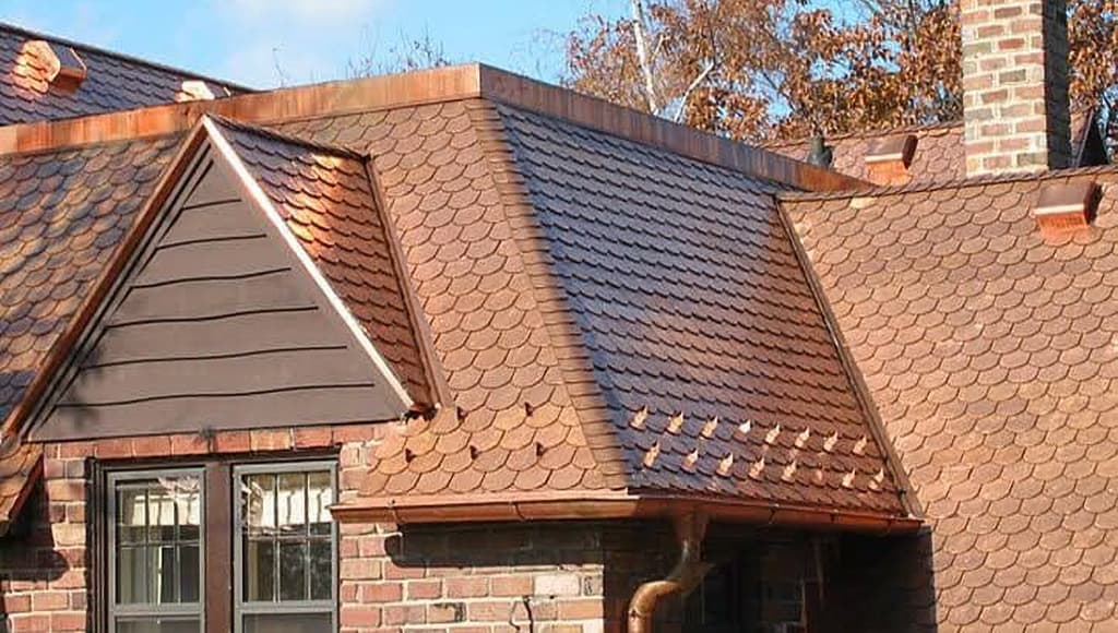 A beautiful copper roof with curved shingles on a brick house