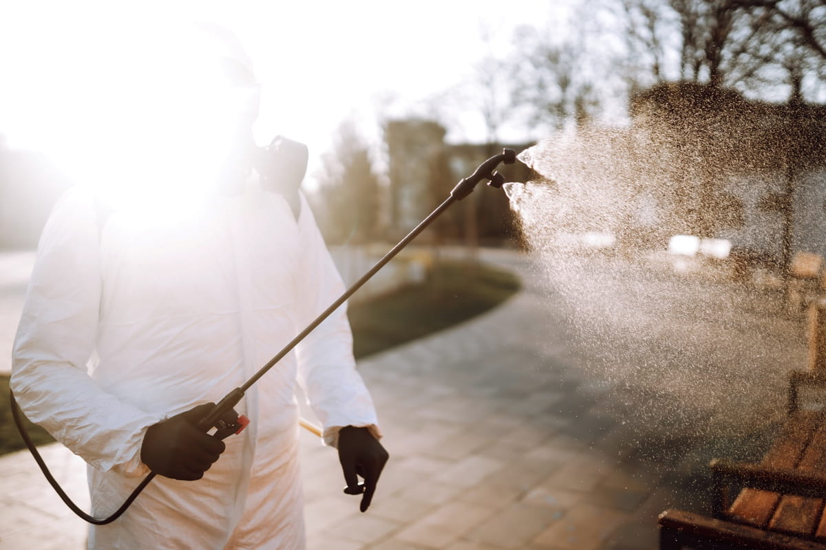 Worker in protective suit using applicator to spray solution