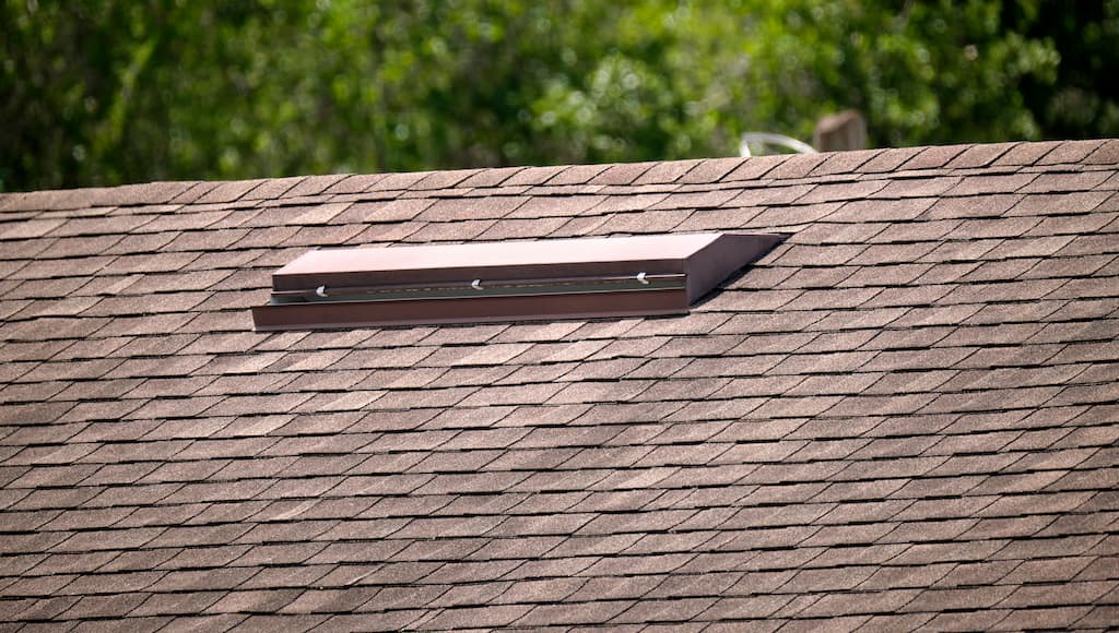 Close-up of a roof vent on a house with asphalt shingles.