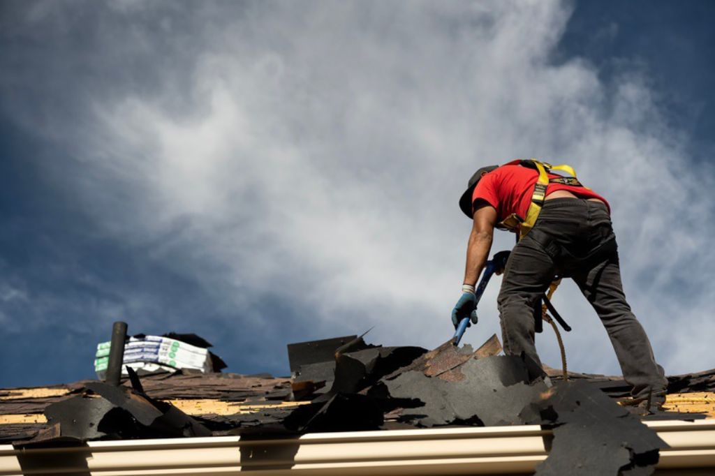 Roofing contractor removing damaged shingles from rooftop that suffered damage in storm