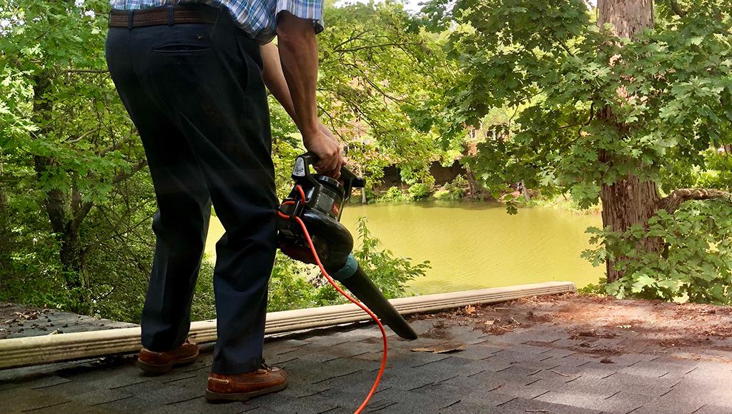 Man using a leafblower to remove leaves from a roof