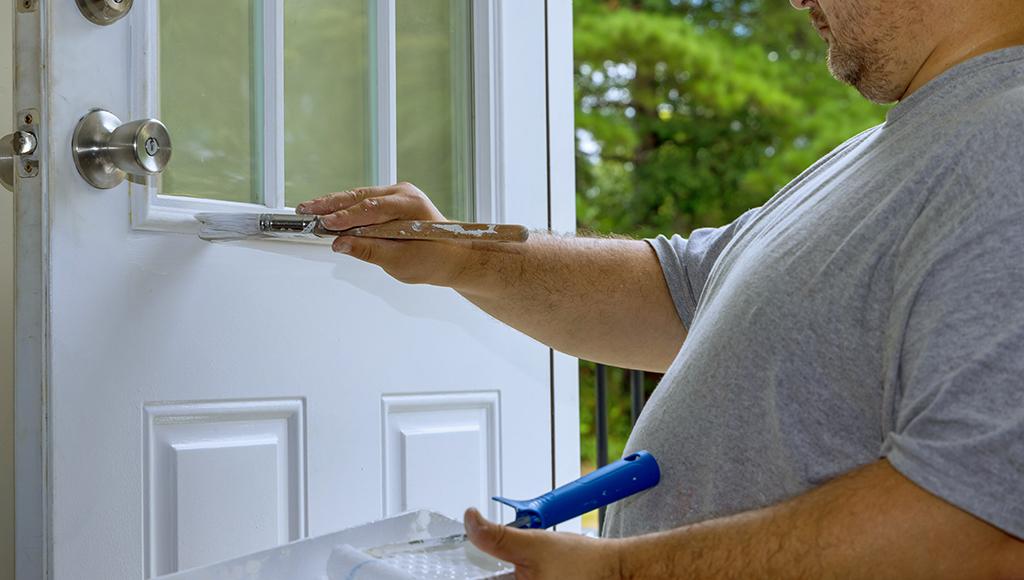 A man applies a fresh coat of paint to an exterior door