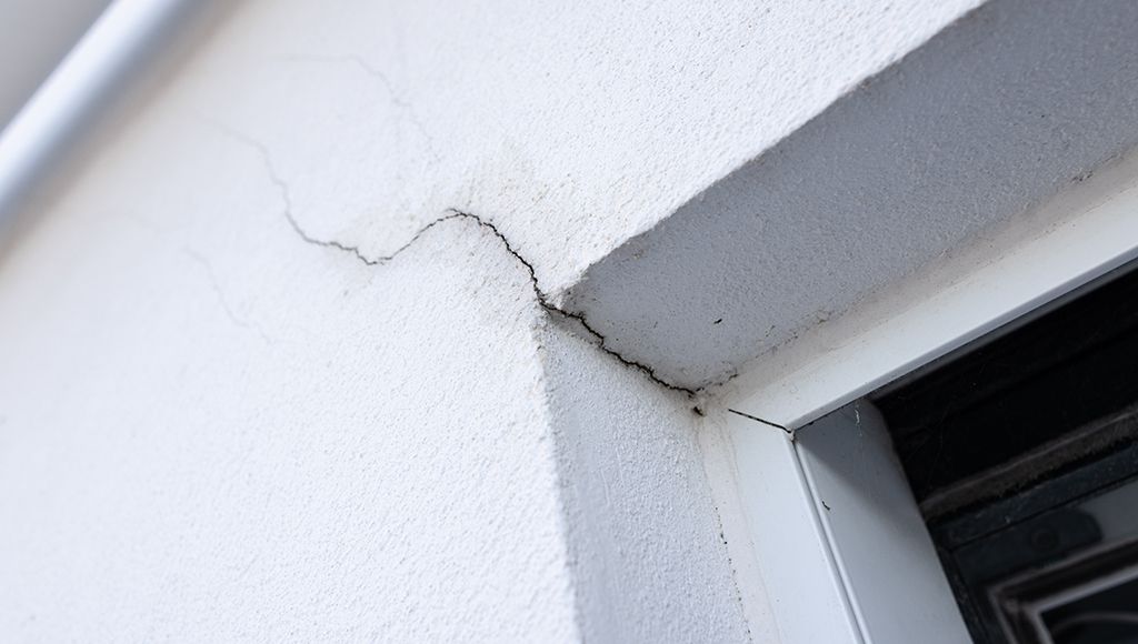 Cracks developing in a concrete foundation around a basement window.