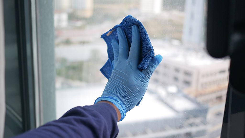 A person cleans a window with a soft blue microfiber cloth.