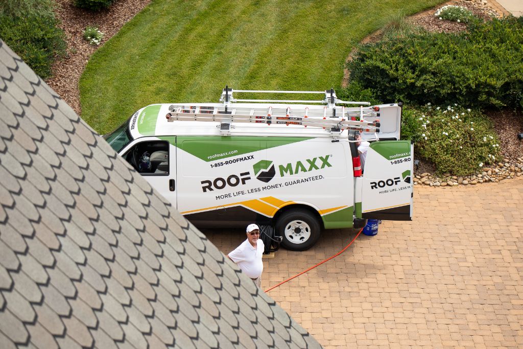 A Roof Maxx dealer stands by a branded van, looking up at a roof.