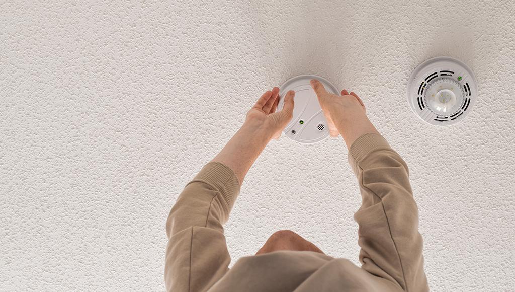 A man removes an old smoke alarm after installing a new one.