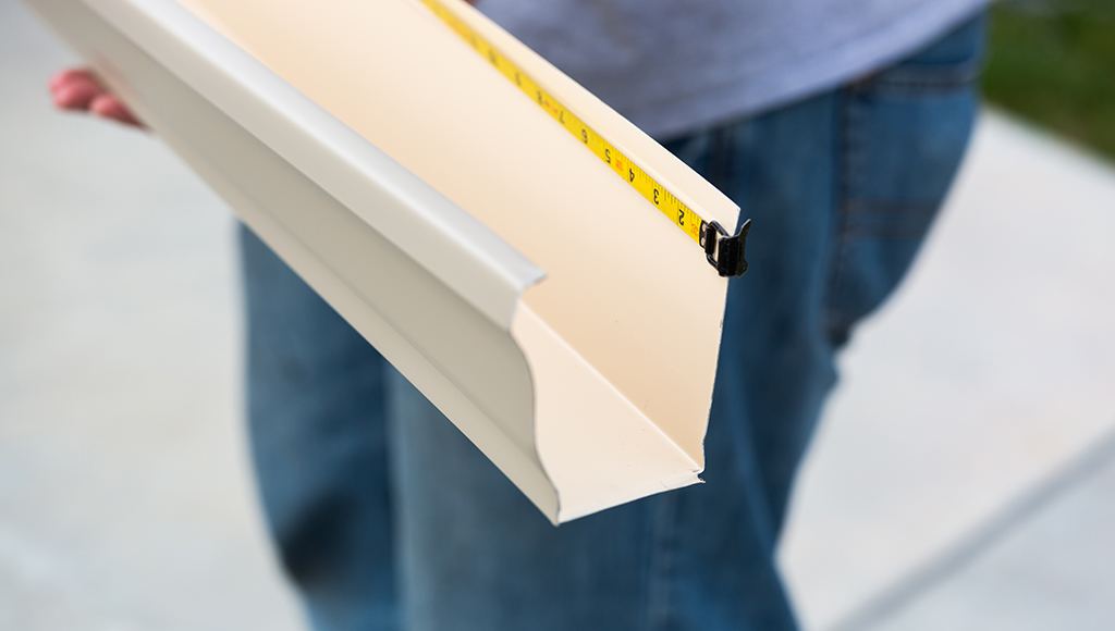 A roofer measures a strip of gutter before installing it on a roof.