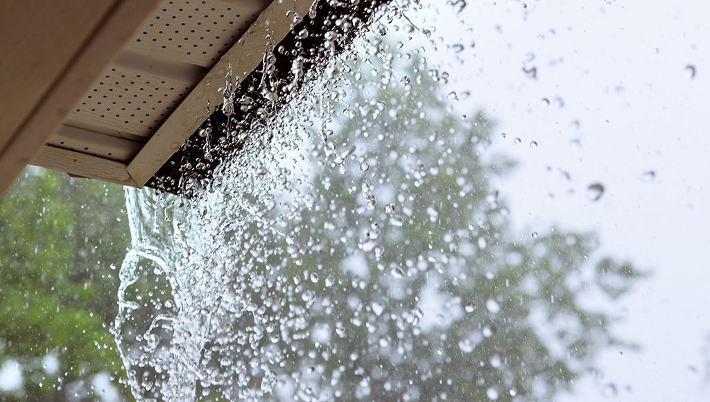 Rain pours off a roof with undersized 5" gutters.