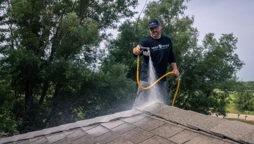 A Roof Maxx dealer spraying a roof on a home near trees with the treatment.