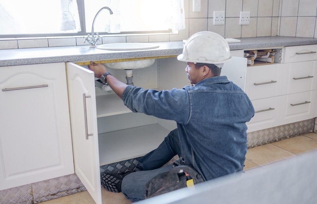 Contractor in hard hat working under the sink as part of service bundle for multiple commercial real estate properties
