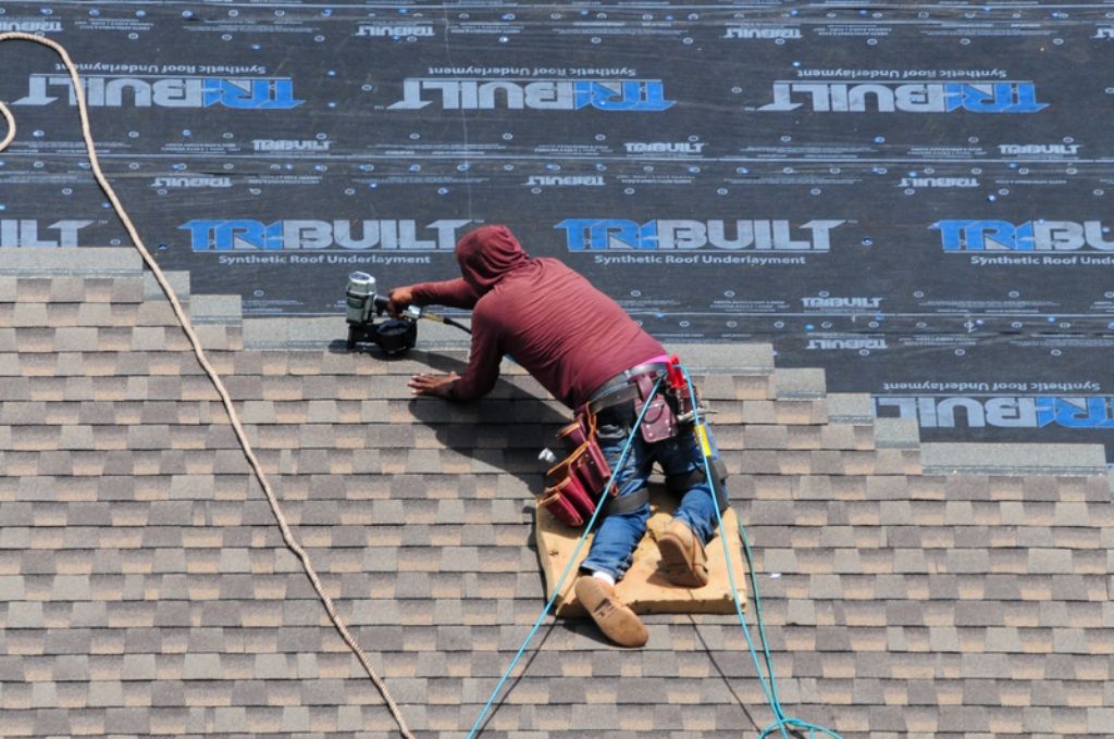 Roofing contractor installing shingles on synthetic roof underlayment