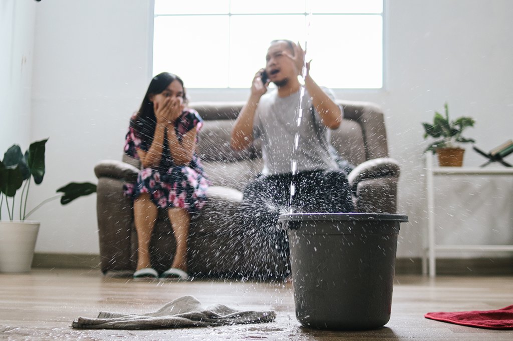 A man and his daughter look on in shock as water pours down from a leak in the roof