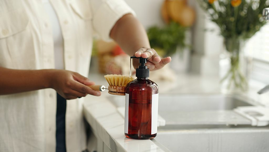 A woman loads up her scrubbing brush with a natural dish soap.