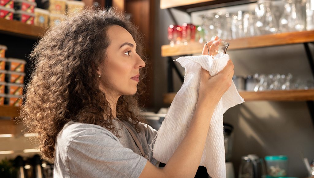 Woman in pantry of home using reusable paper towels to clean glassware