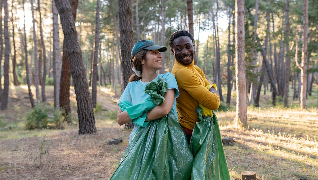 A woman and a man use compostable trash bags to pick up leaves and branches in the yard.