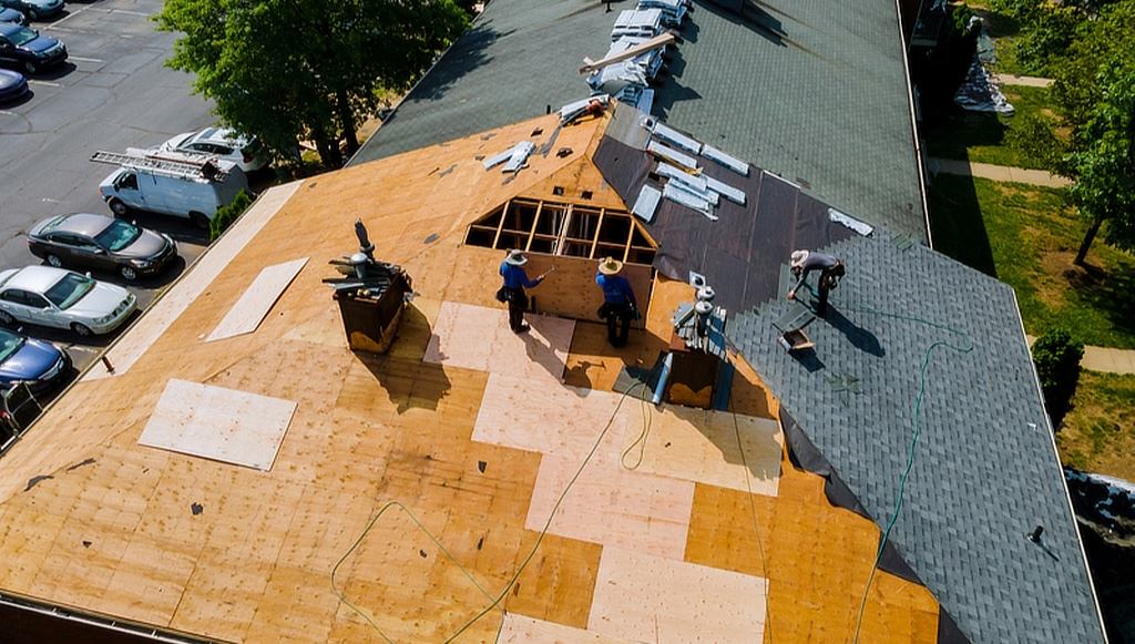 Construction workers removing asphalt shingles and underlayment from a roof.
