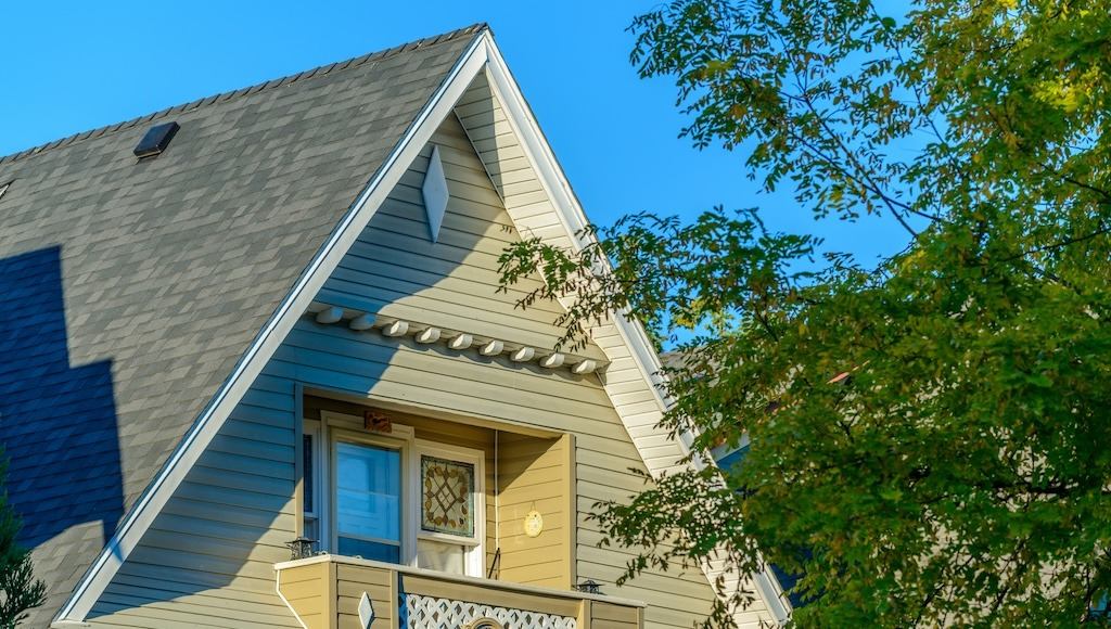 A tall peaked roof on a green residential home with asphalt shingles.