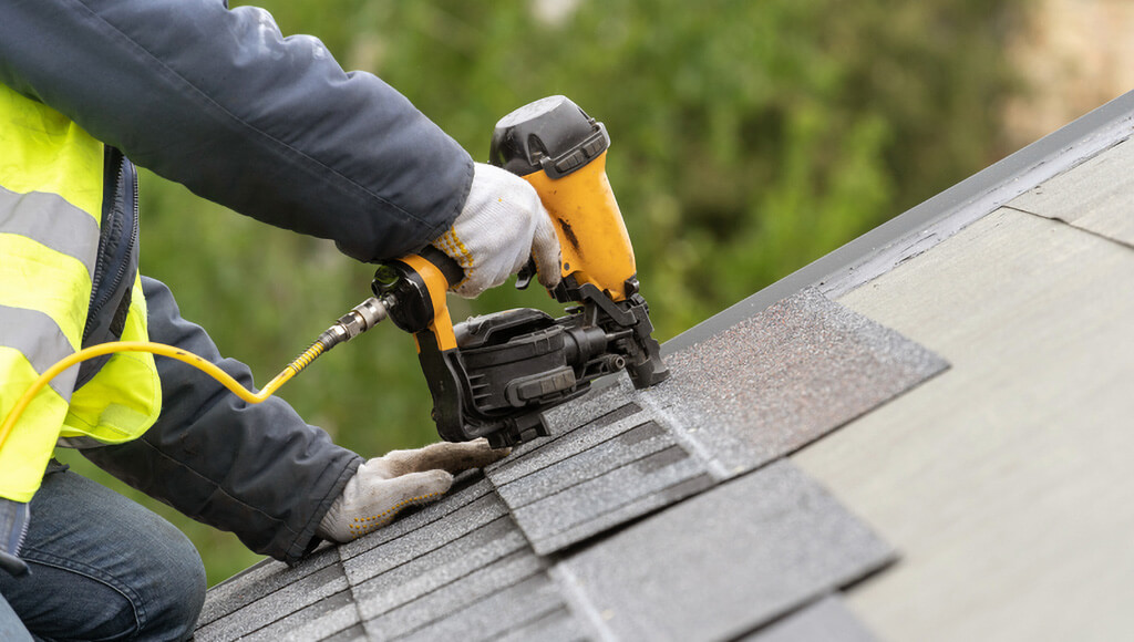 A roofer installs new shingles over a patch of missing shingles.