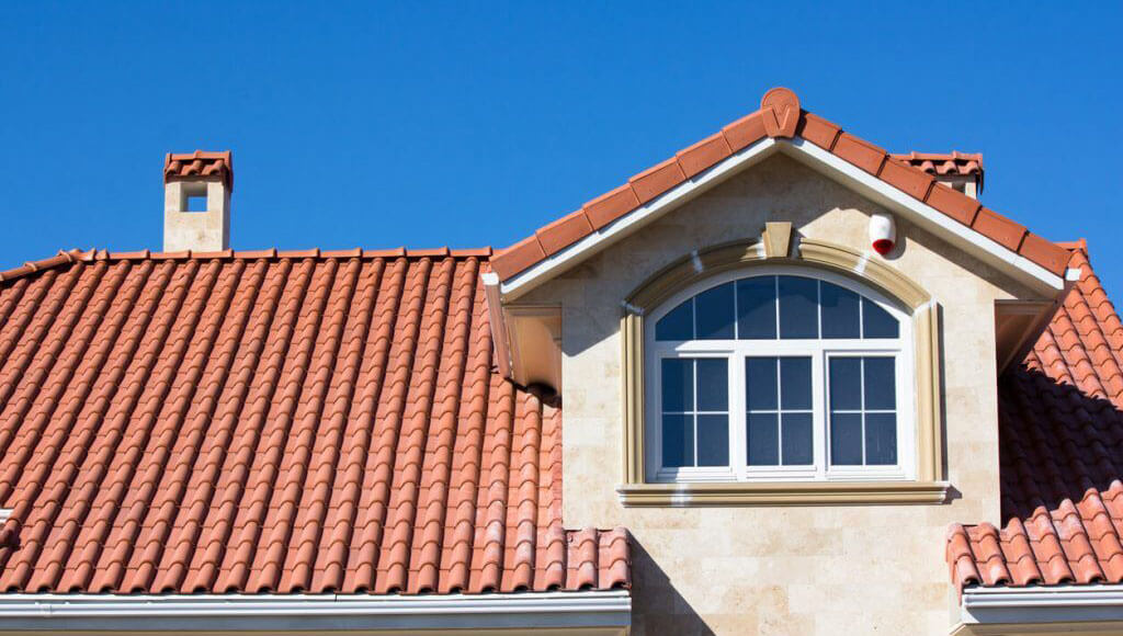 A clay tile roof on a Spanish-style residential home with a decorative dormer window.