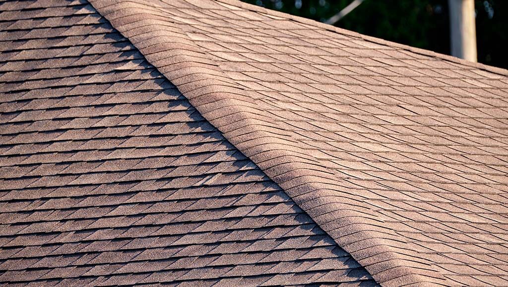 Closeup of a red asphalt shingle roof ridge.