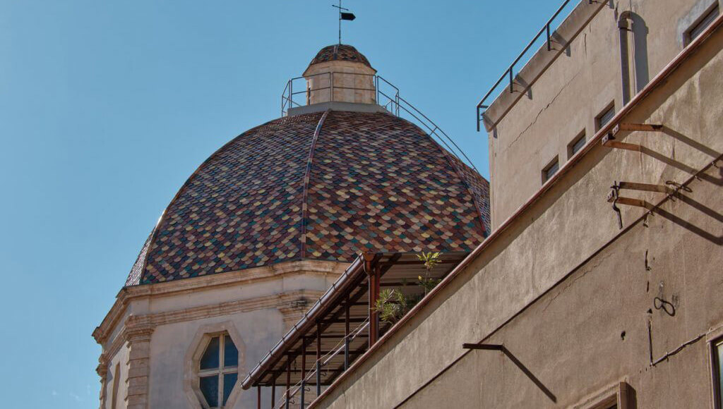 A domed copper and multicolored tile roof on a church steeple against a clear blue sky.