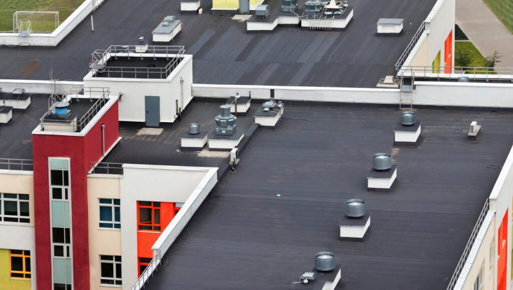 Top-down view of a flat bitumen roof on a colorful commercial or apartment complex with multiple HVAC vents.