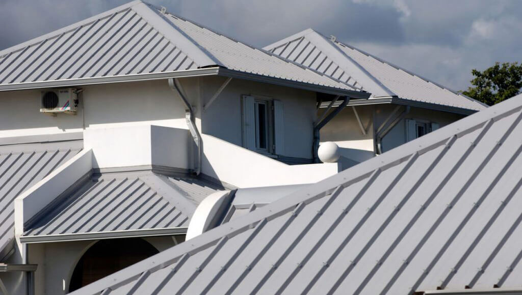 A grey metal panel roof on a modern residential home with multiple roof sections and an air conditioning unit.