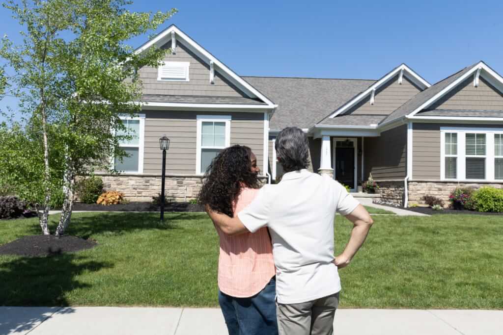 Two happy homeowners stand in front of their home and review the results of their Roof Maxx treatment from the curb.