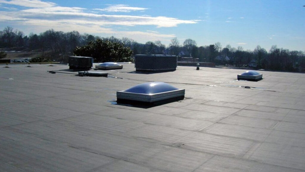 Skylights installed on a flat EPDM roof next to large vents and HVAC equipment.