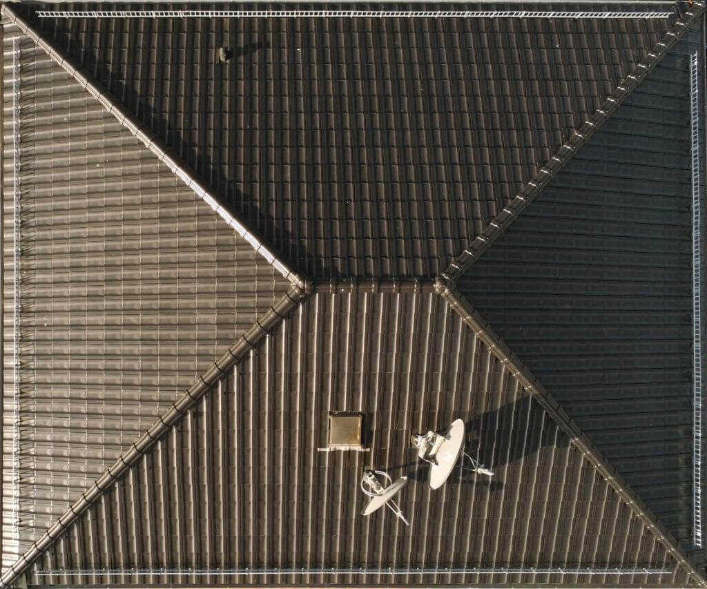 Top-down aerial view of a dark tiled hipped roof with satellite dishes and a chimney.