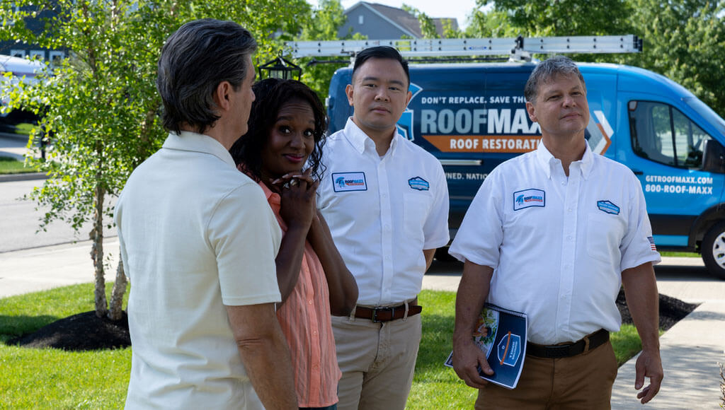 Two male Roof Maxx dealers chat with a couple in front of their house.