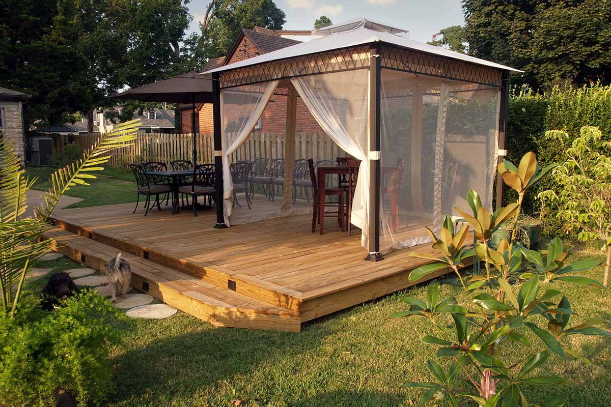 A backyard cabana with furniture, lighting and mosquito net curtains to ward off pests.
