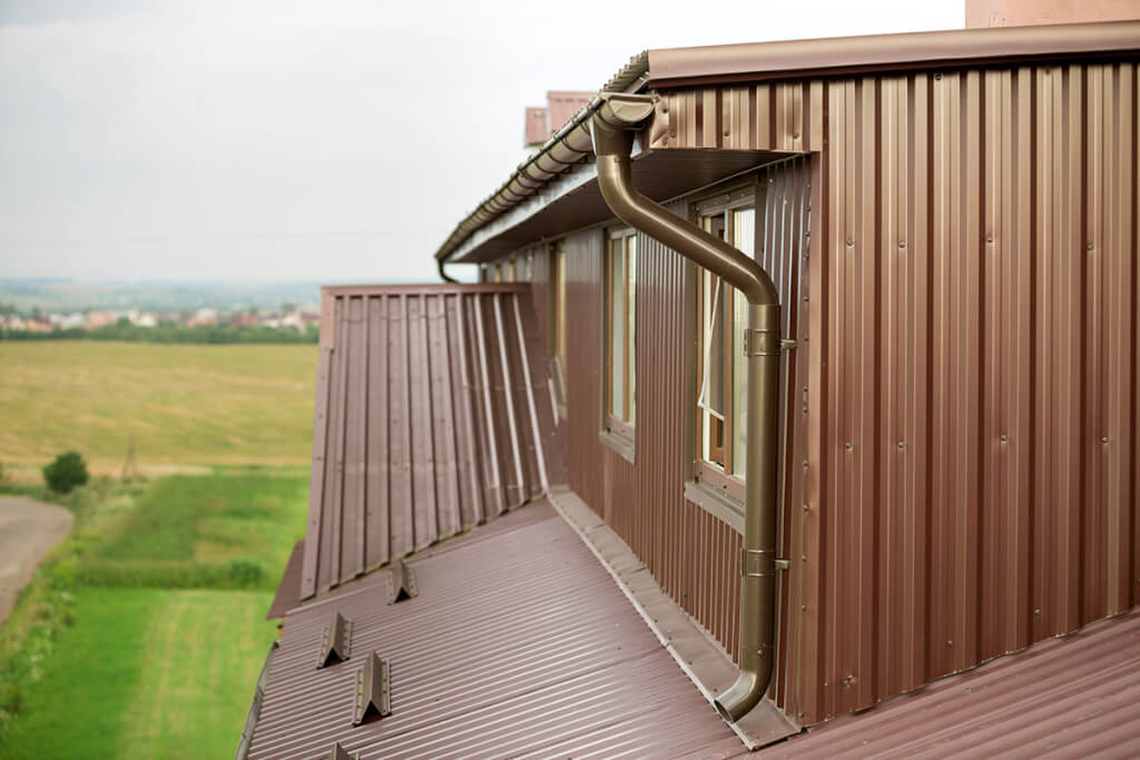 Metal gutters and downspouts on a home with brown corrugated metal siding and roofing.