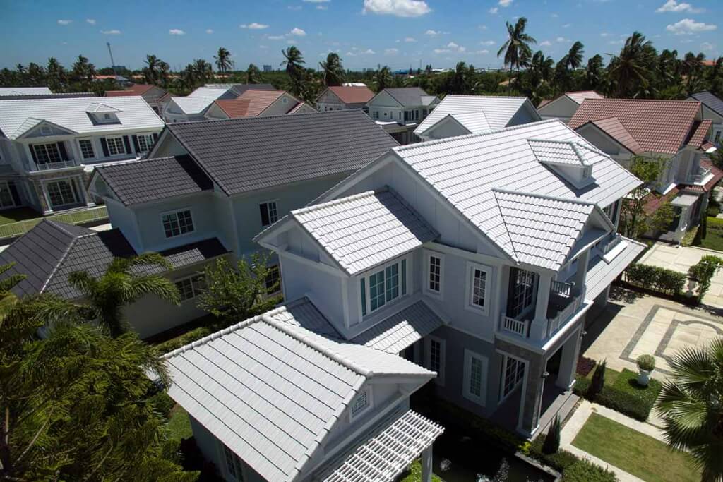 Aerial view of molded metal roofs on large residential homes in a tropical coastal neighborhood surrounded by palm trees.