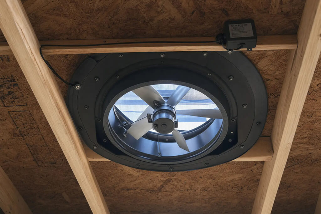 A large, round powered attic ventilation fan attached to the underside of roof decking.