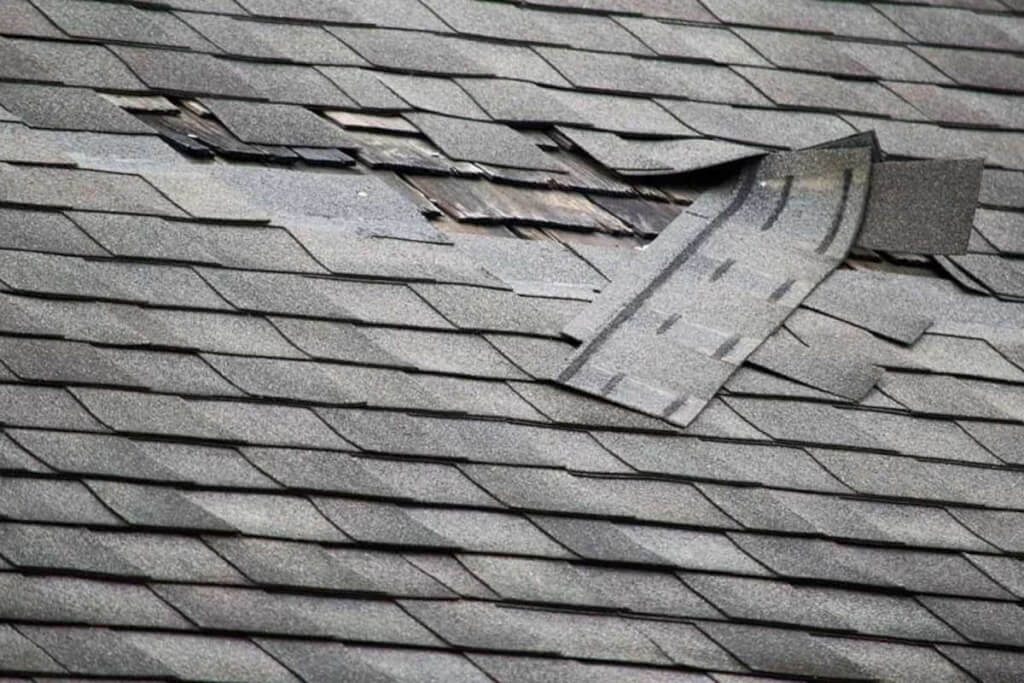 Damaged asphalt shingles are cracked, loose, and missing from part of a residential roof.