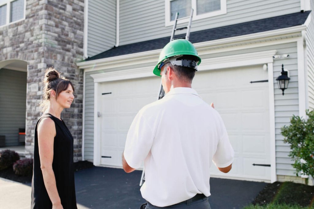 A Roof Maxx dealer in a green hard hat gets ready to inspect a customer's roof while speaking with a homeowner.