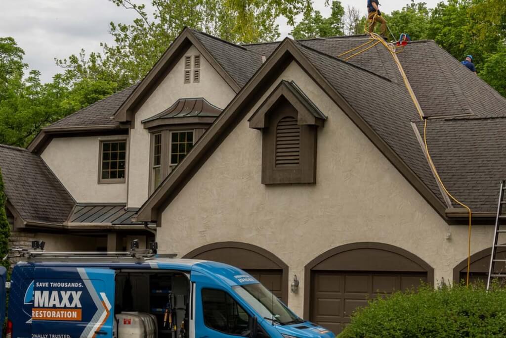 Two Roof Maxx dealers stand on a customer's asphalt shingle roof.