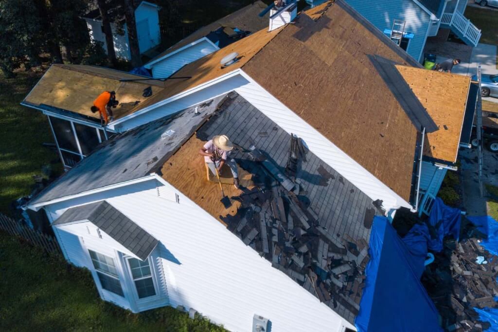 Roofers work on tearing the shingles off an asphalt shingle roof.
