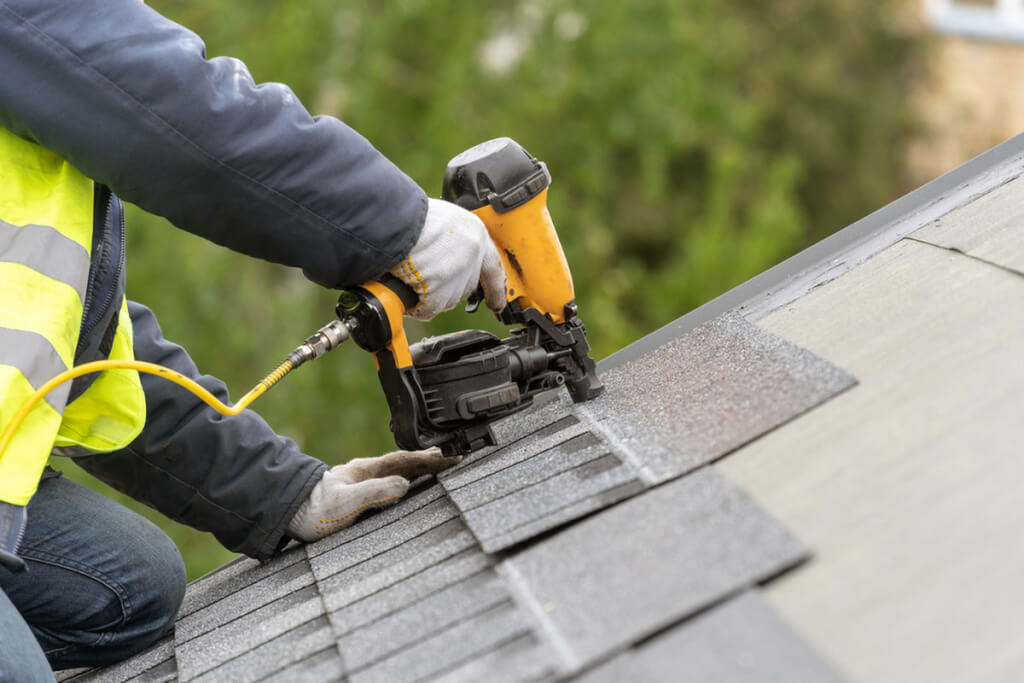 A roofer installs new shingles over a patch of missing shingles.
