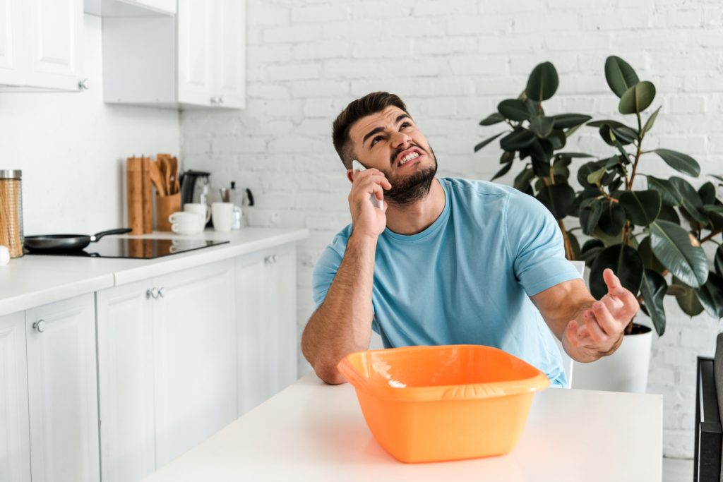 angry bearded man talking on smartphone near plastic wash bowl